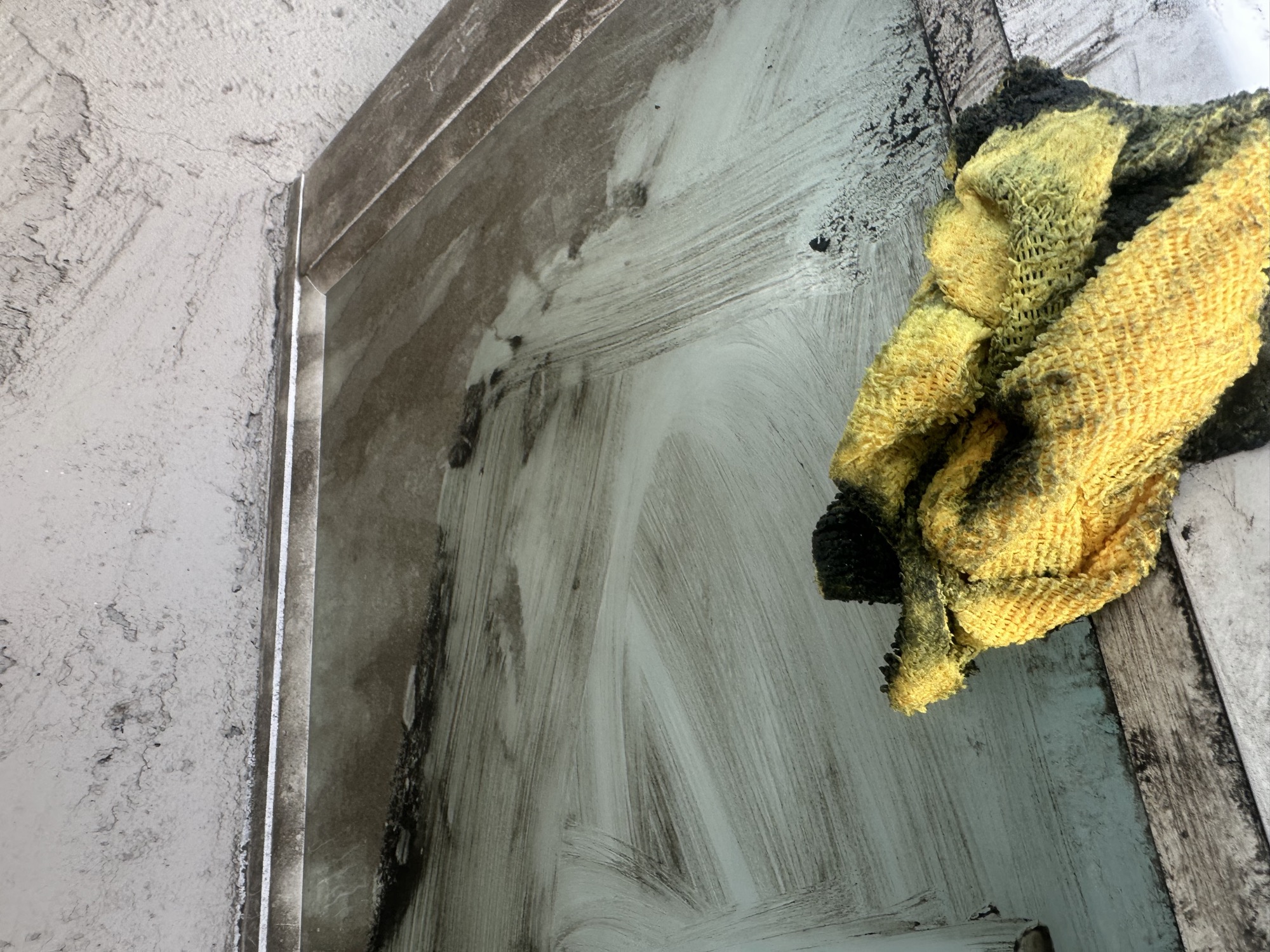 A heavily soiled window mid-scrub, cleaning rag resting on the glass